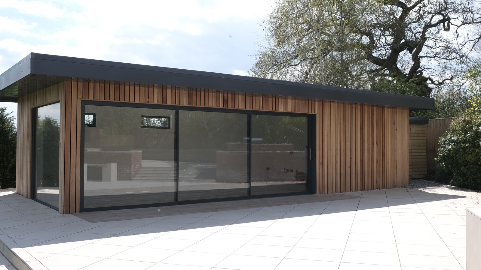 Completed cedar-clad garden room with sliding glazed doors and porcelain terrace