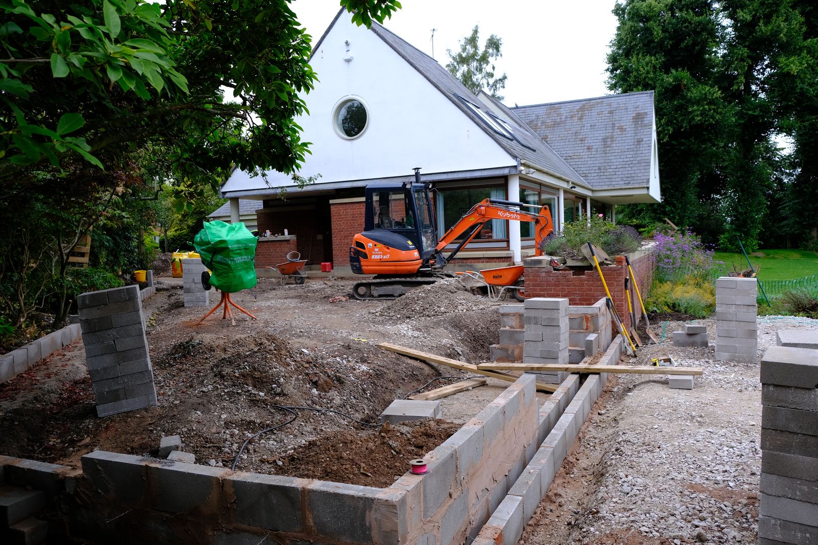 Excavator working beside a house with new retaining walls under construction