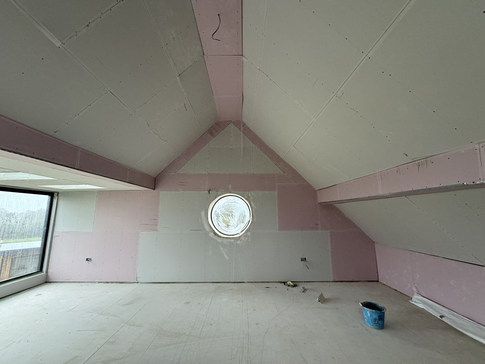 Newly plasterboarded room with a round window and vaulted ceiling