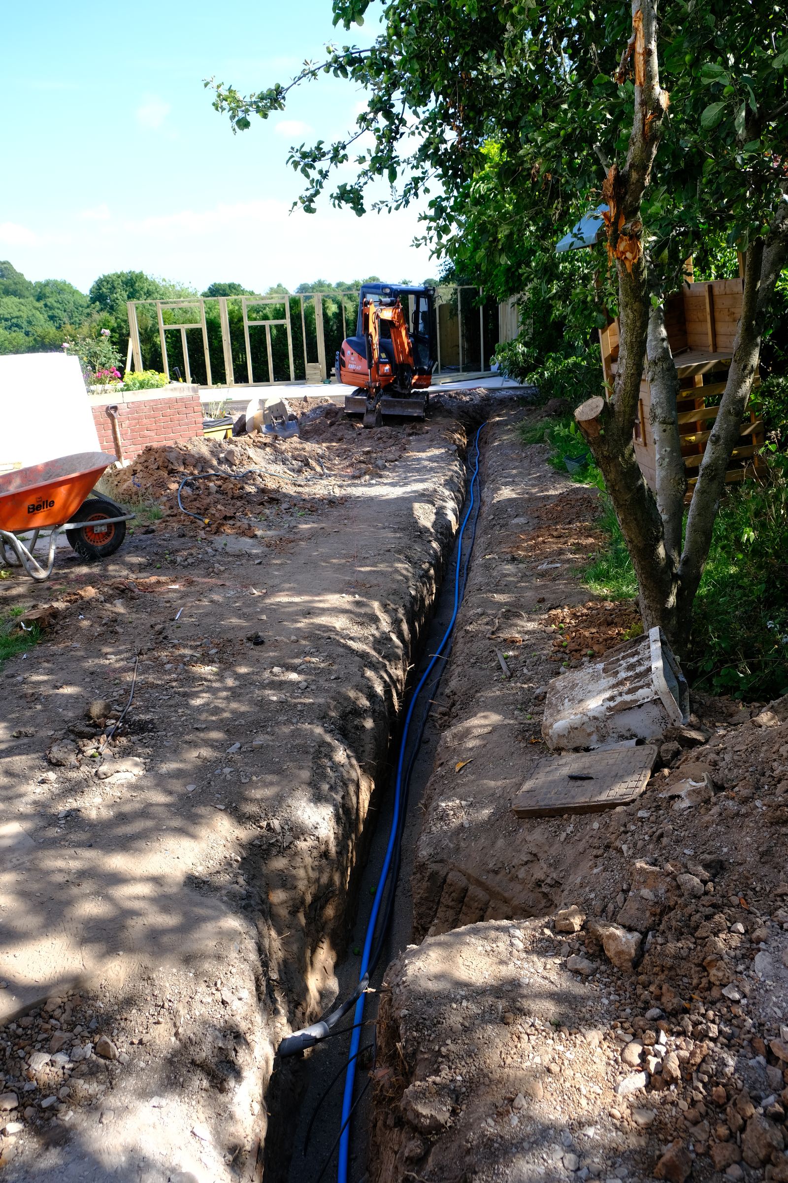 Open trench with water main and ducting laid alongside a new building