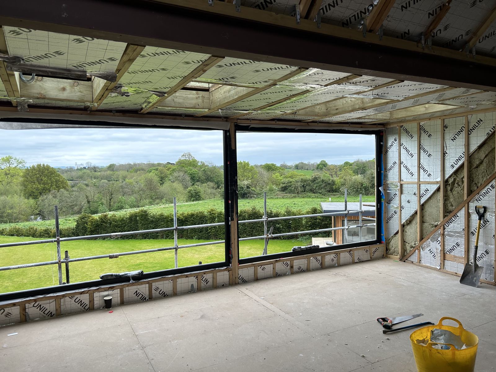 Large window opening formed in an insulated timber frame, looking out over fields